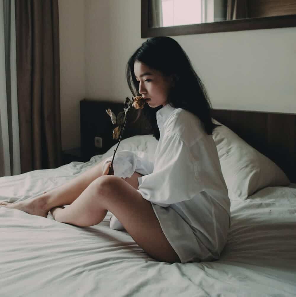 Heartbroken girl in bed holding a rose